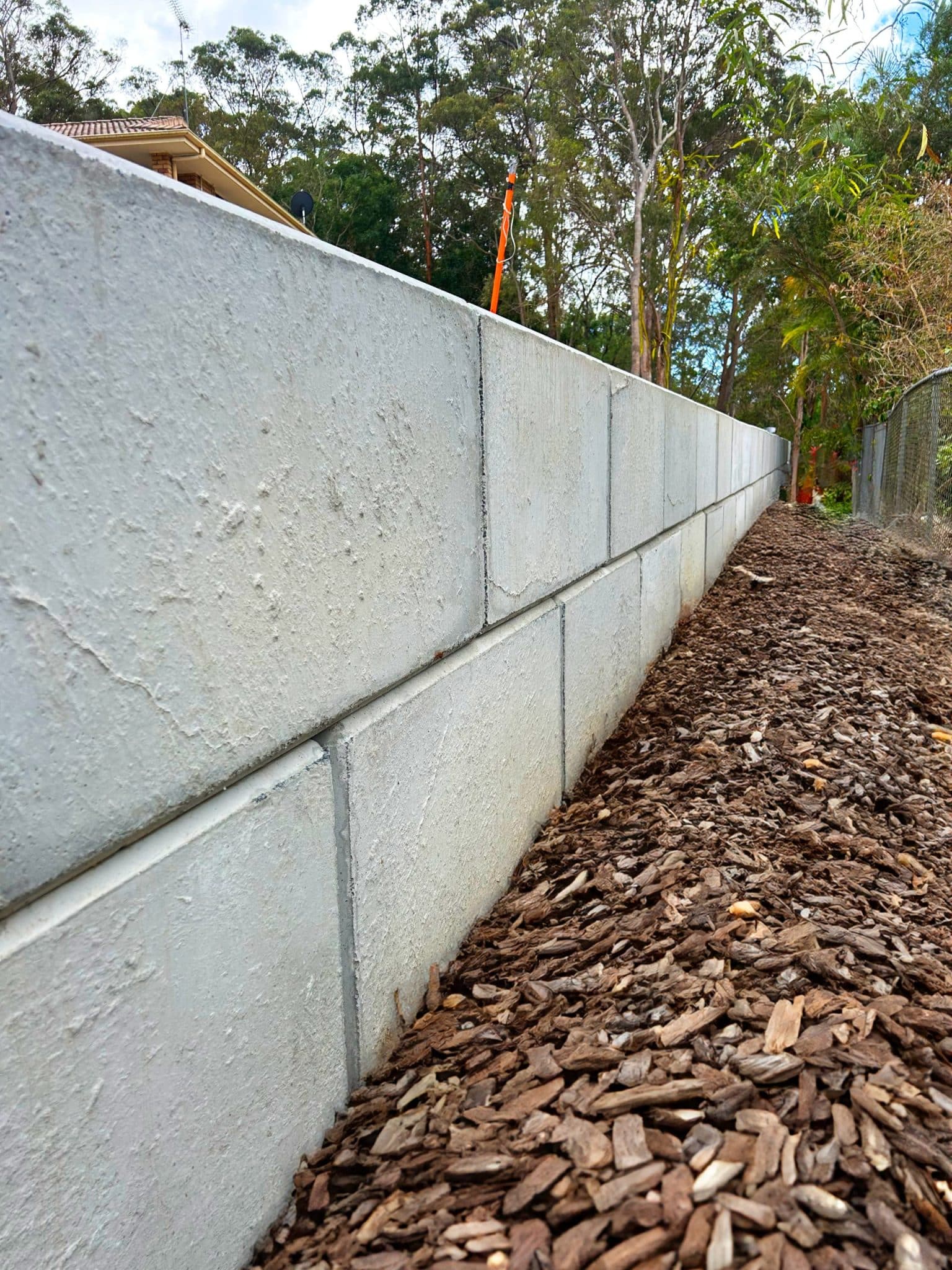 A concrete block retaining wall with mulch at its base, showcasing the durability of concrete blocks vs brick walls in a lush Australian backyard setting.