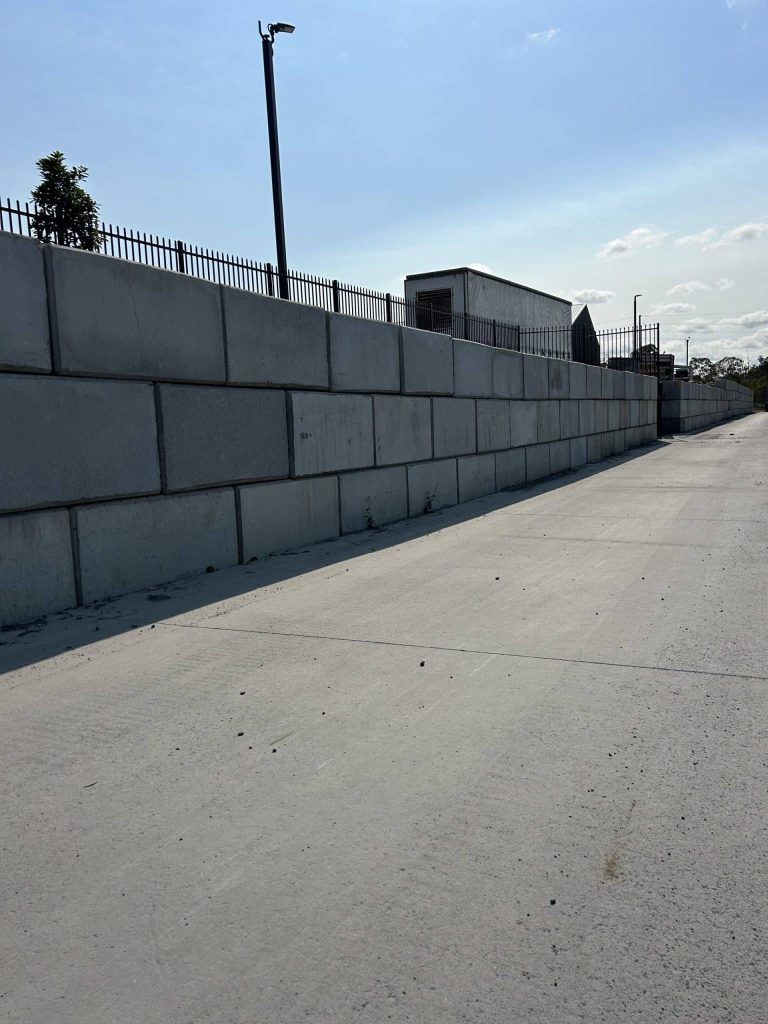 A tall concrete block retaining wall along a paved path, illustrating the strength of concrete blocks vs brick walls in a modern infrastructure setting.