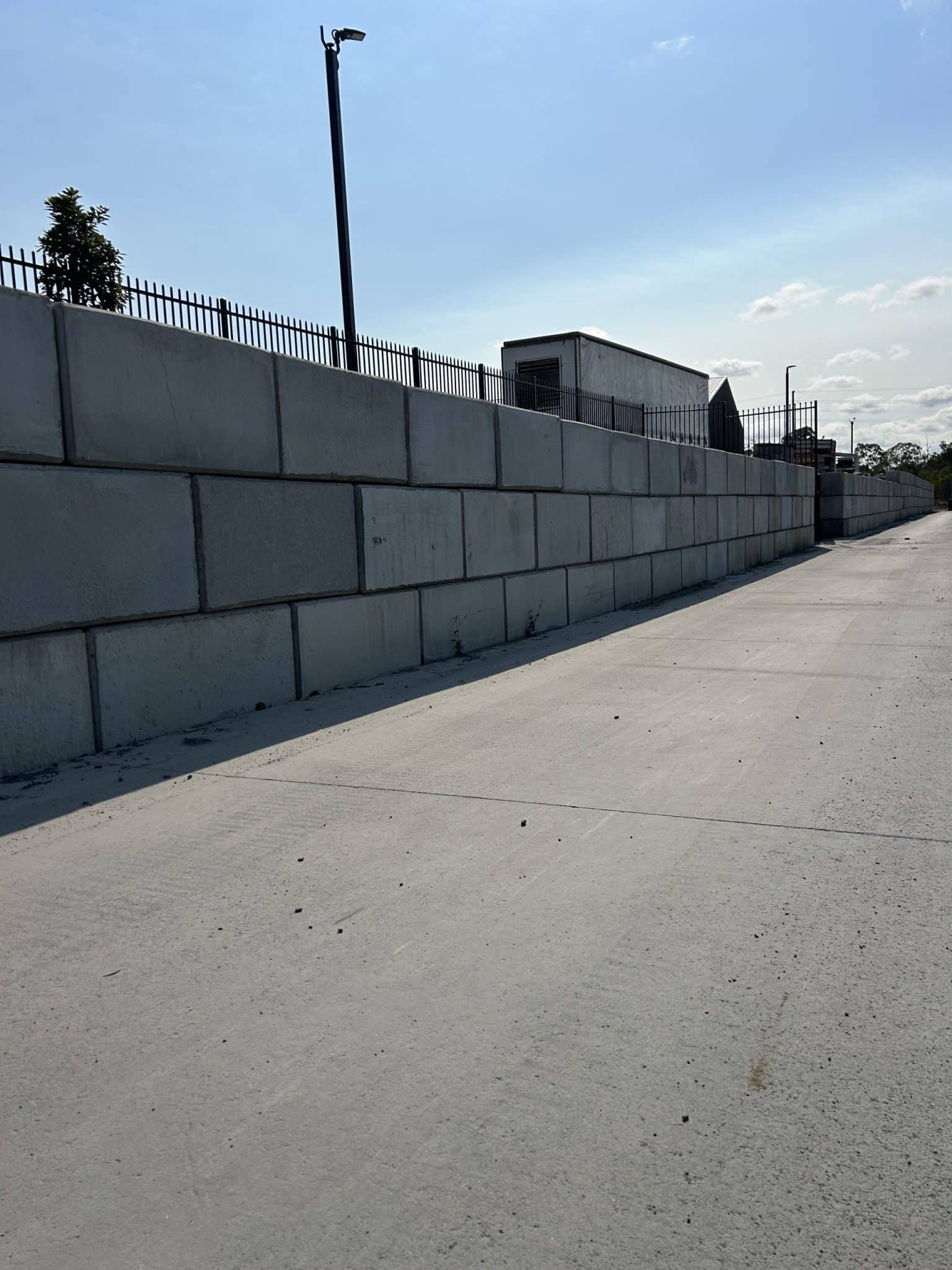 A tall concrete block retaining wall along a paved path, illustrating the strength of concrete blocks vs brick walls in a modern infrastructure setting.