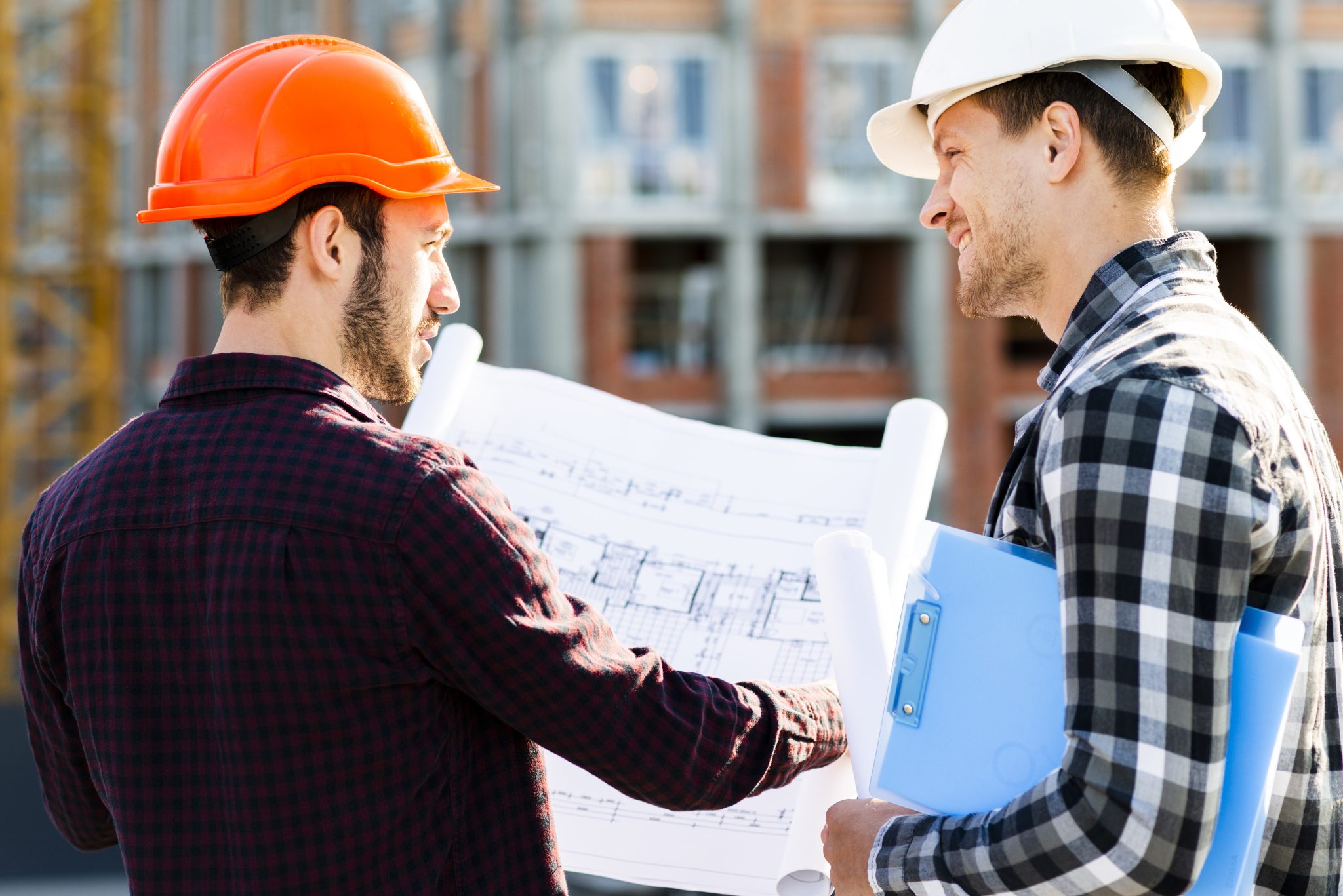 Two licensed contractors in Australia wearing hard hats and discussing construction blueprints at a building site.