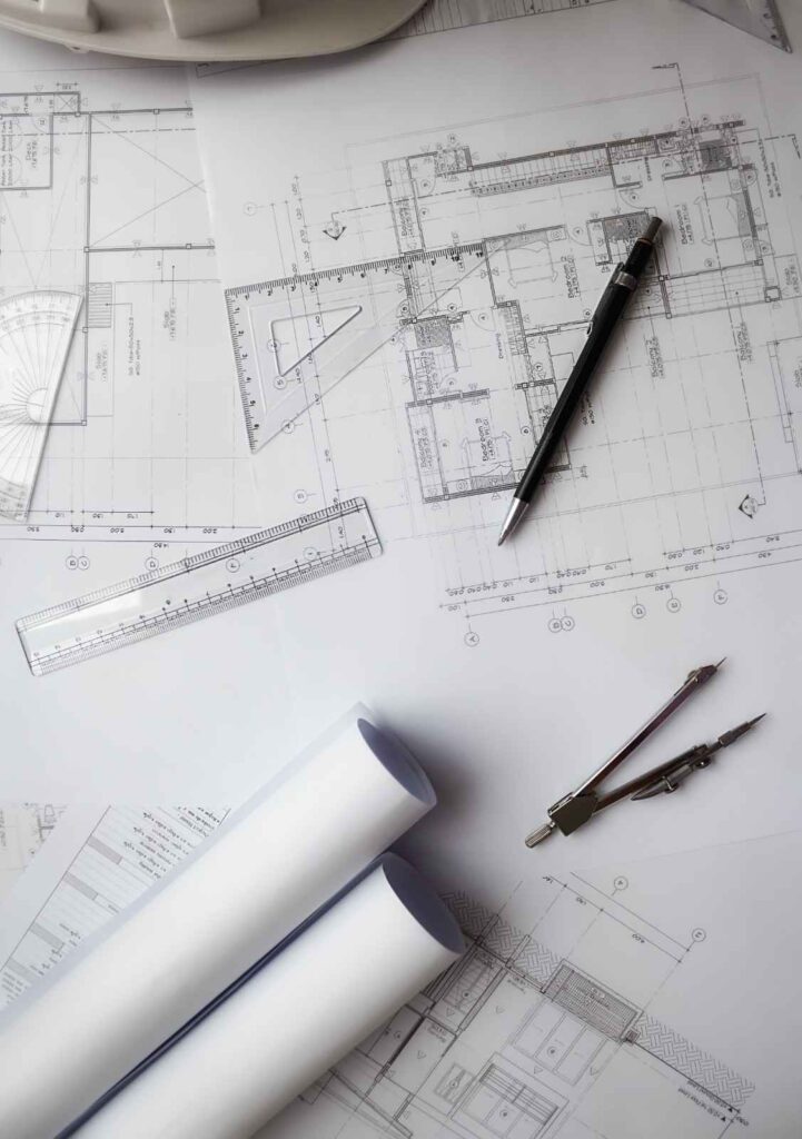 Construction blueprints with rolled-up plans, a pen, compass, and rulers on a workspace, symbolizing architectural planning