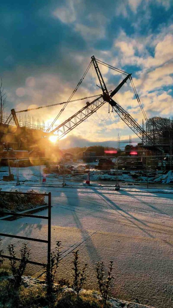 Construction crane on a frosty winter site at sunrise, showcasing the efficiency of precast concrete for winter construction projects.