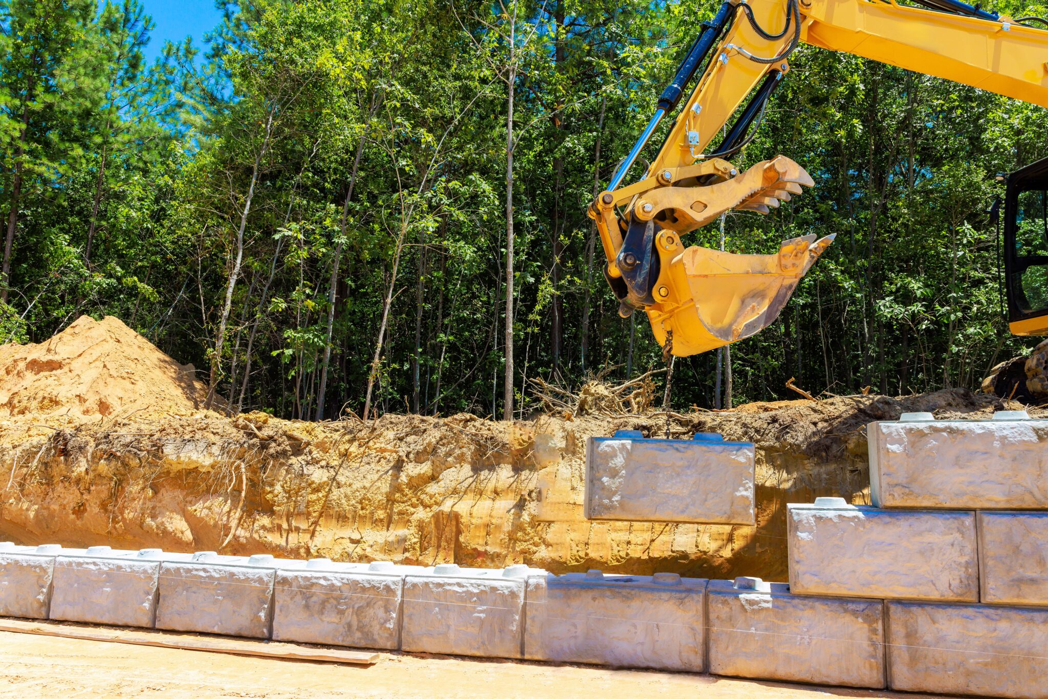 Heavy equipment placing large blocks for a retaining wall showing the benefits when you plan your retaining wall in winter