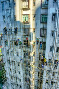 Construction workers assembling bamboo scaffolding on a high-rise building, highlighting traditional methods compared to modern precast concrete in fire-resistant construction.
