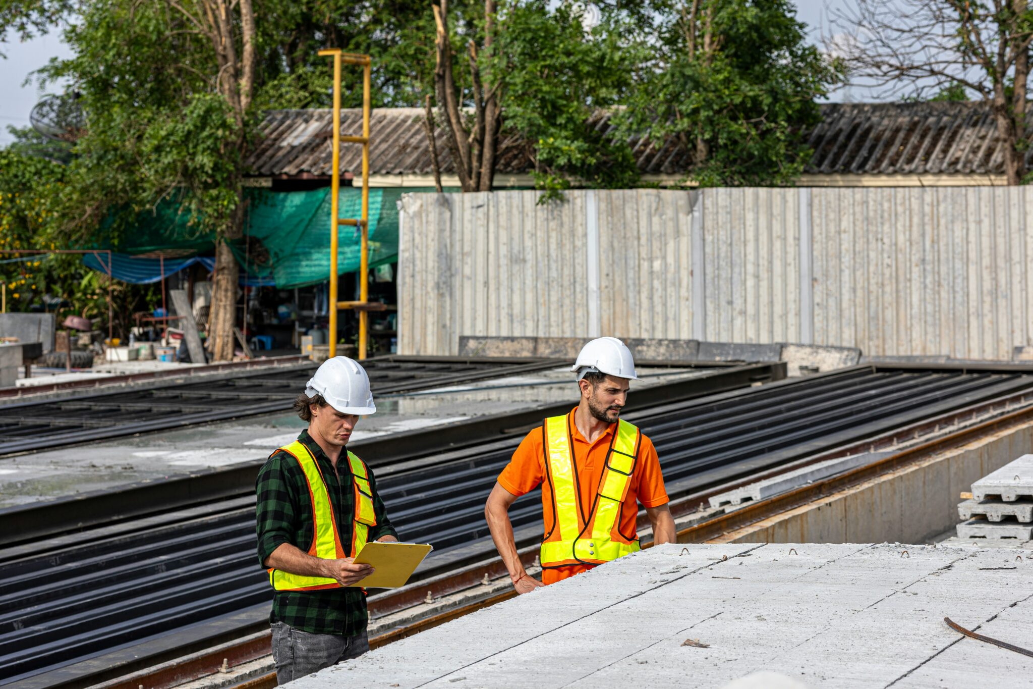 Two construction engineers wearing safety helmets and reflective vests inspecting precast concrete panels at a building site on the Gold Coast for spring builds.