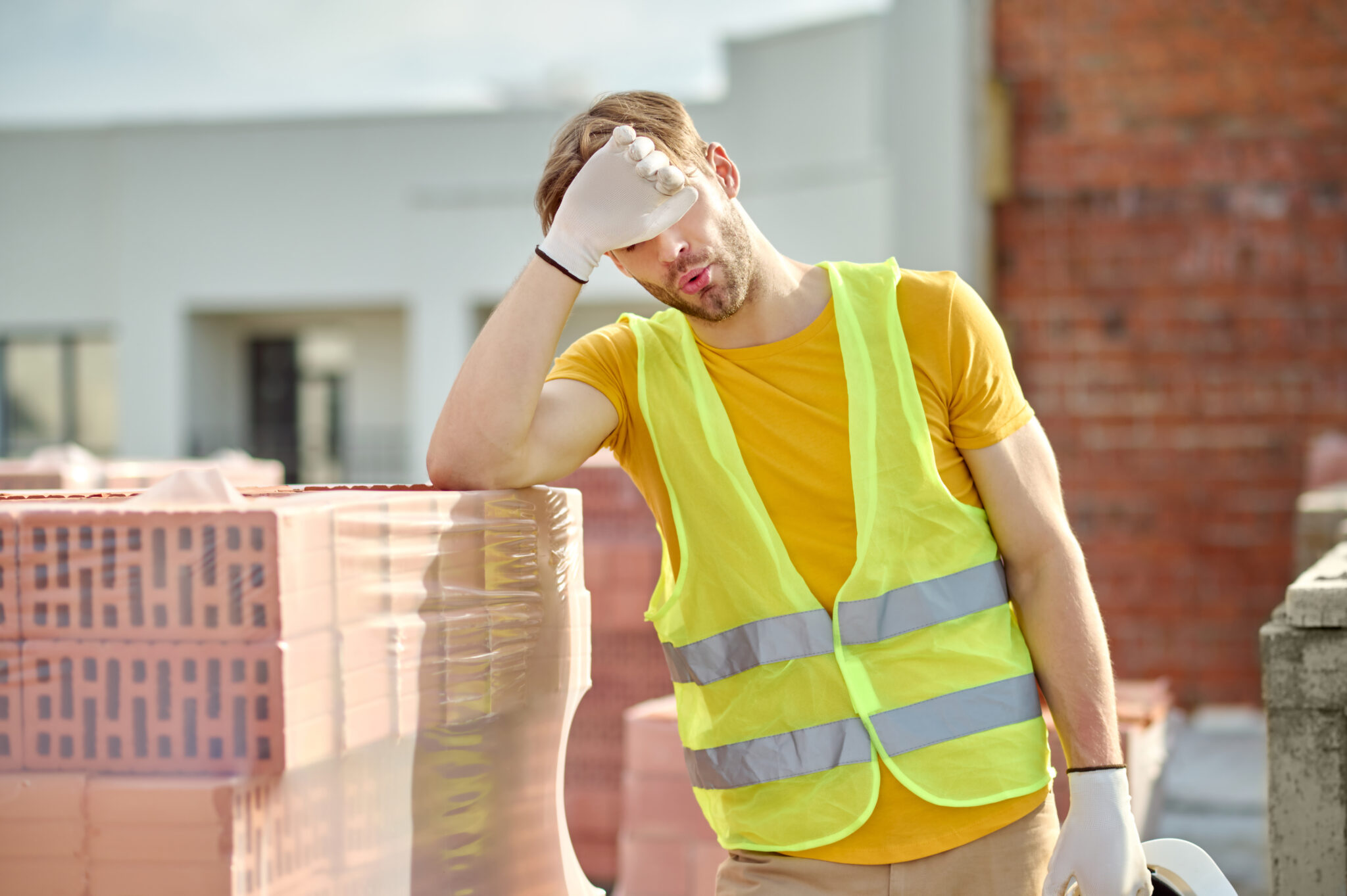 Tired construction worker in a safety vest taking a break beside stacked bricks during precast concrete construction on the Gold Coast.