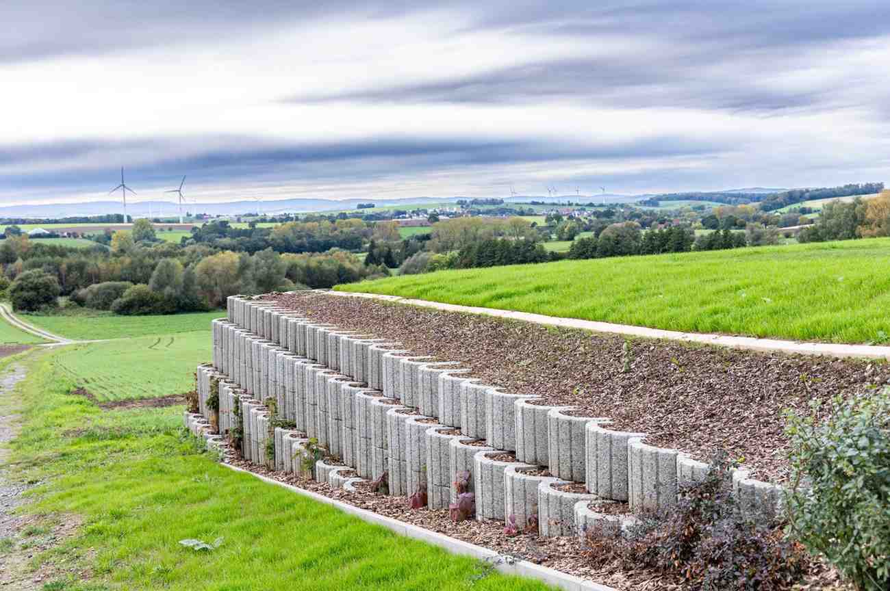 Tiered concrete retaining walls supporting a landscaped slope with green grass and countryside views, demonstrating retaining walls for sloped backyards on the Gold Coast.