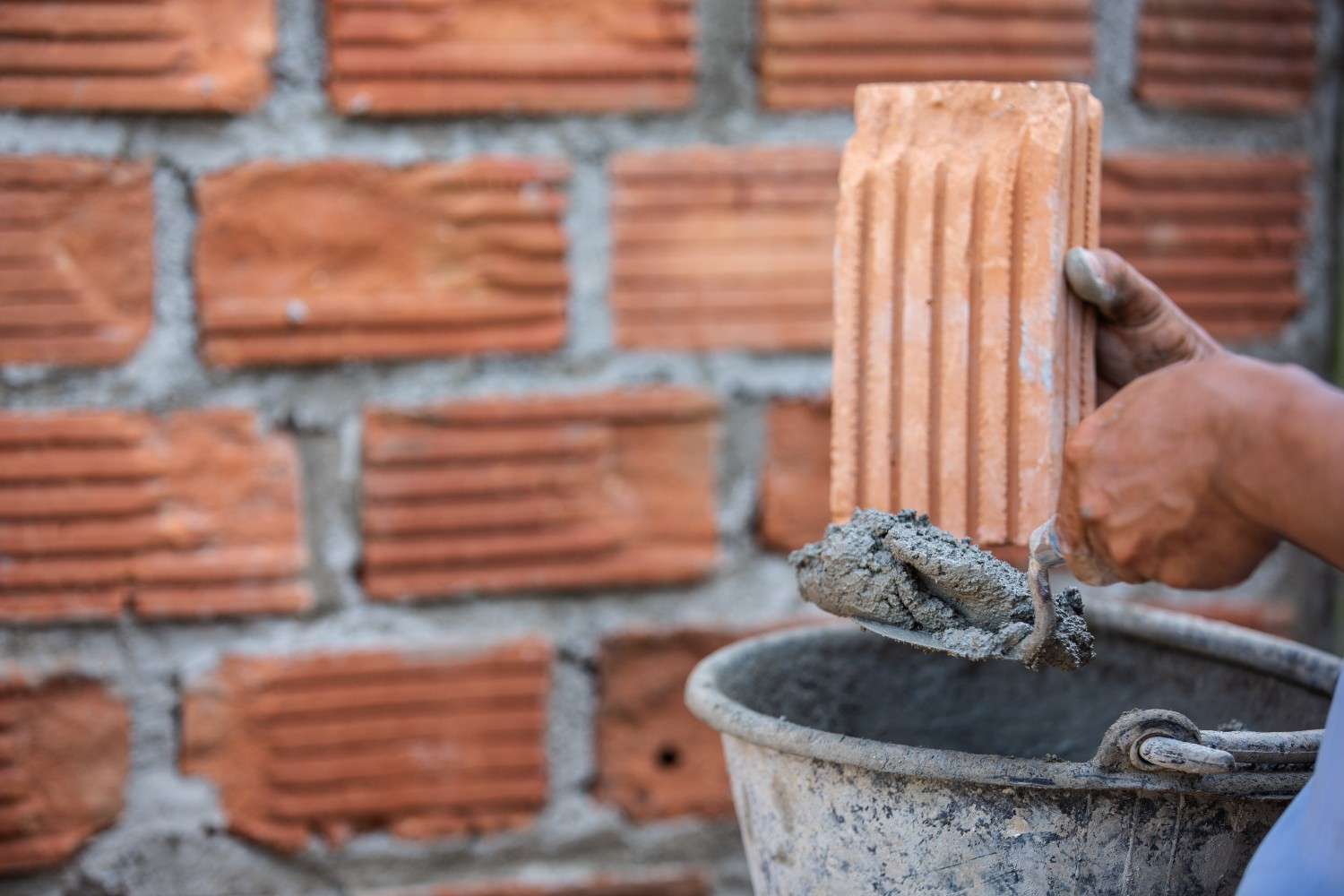 Masonry worker applying mortar during brick installation as precast retaining wall