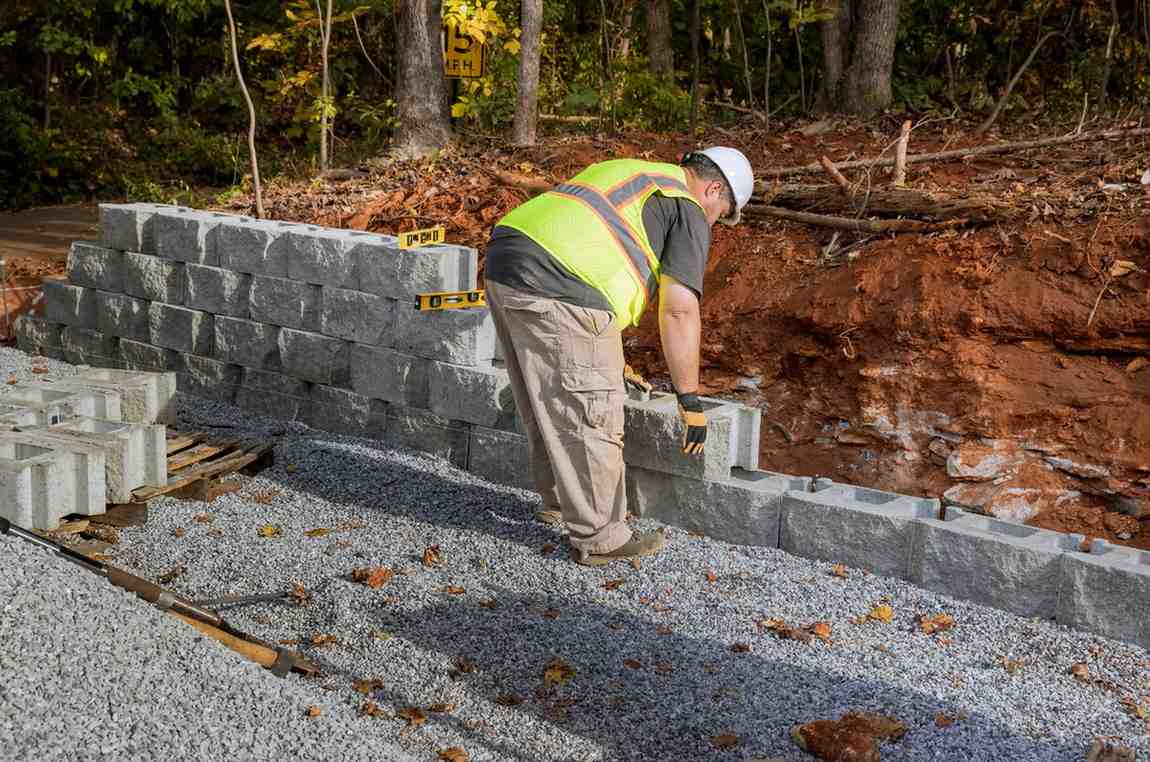 Retaining wall construction on the Gold Coast with worker installing concrete blocks on a prepared gravel base