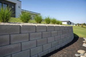 Retaining walls for sloped land using modern concrete blocks with ornamental grasses and gravel landscaping.