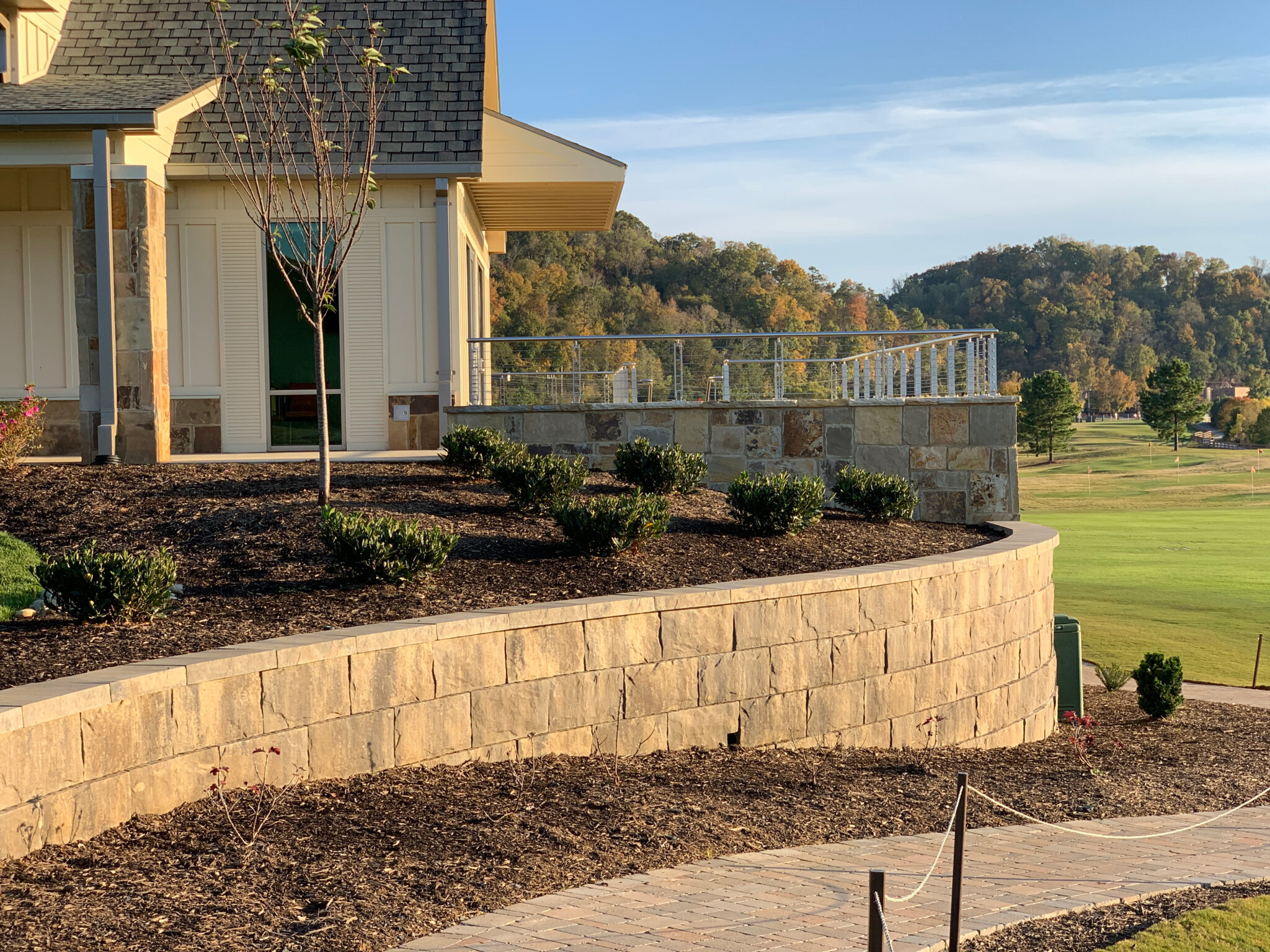Retaining walls for sloped land made with natural stone to support landscaped beds near a hillside property.