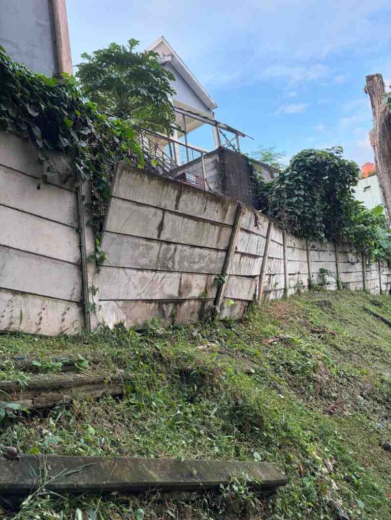 Emergency retaining wall leaning and separating on a slope below a house after heavy rain