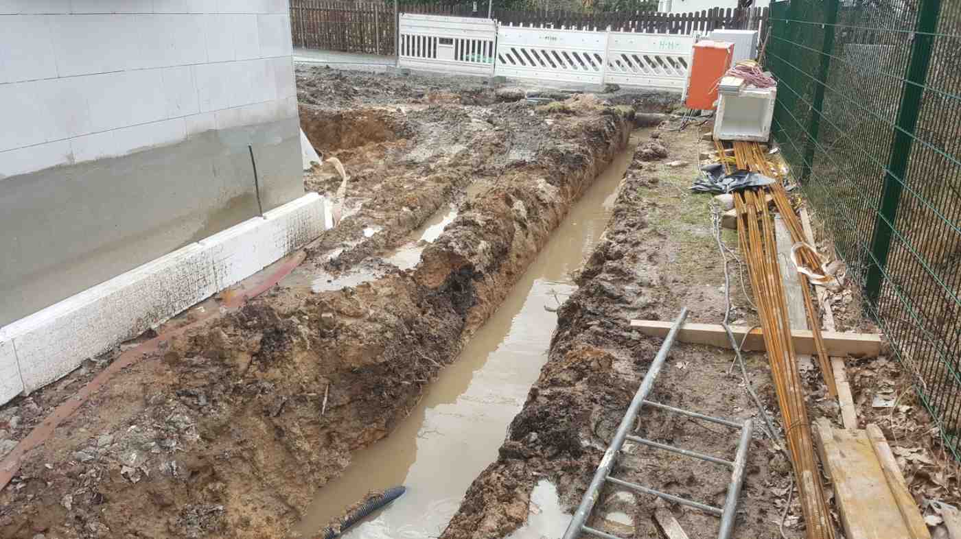 Flooded trench filled with muddy water beside a partially built wall on a waterlogged construction site