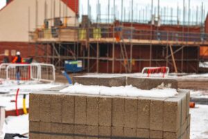 Stack of precast concrete blocks on a winter construction site, with scaffolding and a brick building behind best time to build retaining walls