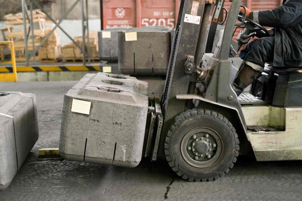 Forklift moving a large precast concrete block in an industrial storage yard