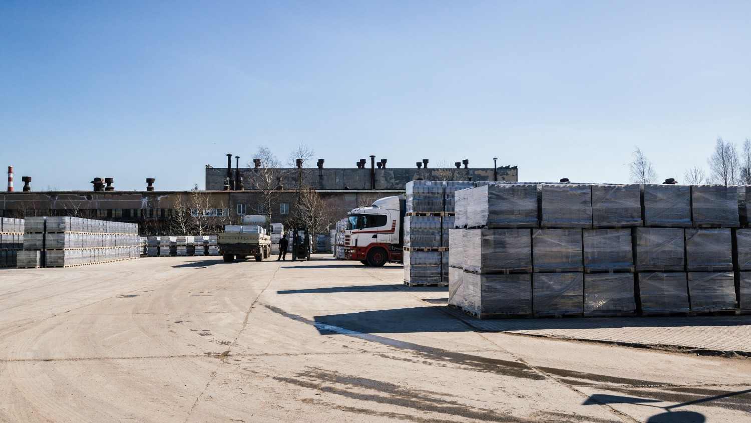 Truck and forklift at a concrete block supply yard with shrink-wrapped pallets ready for dispatch
