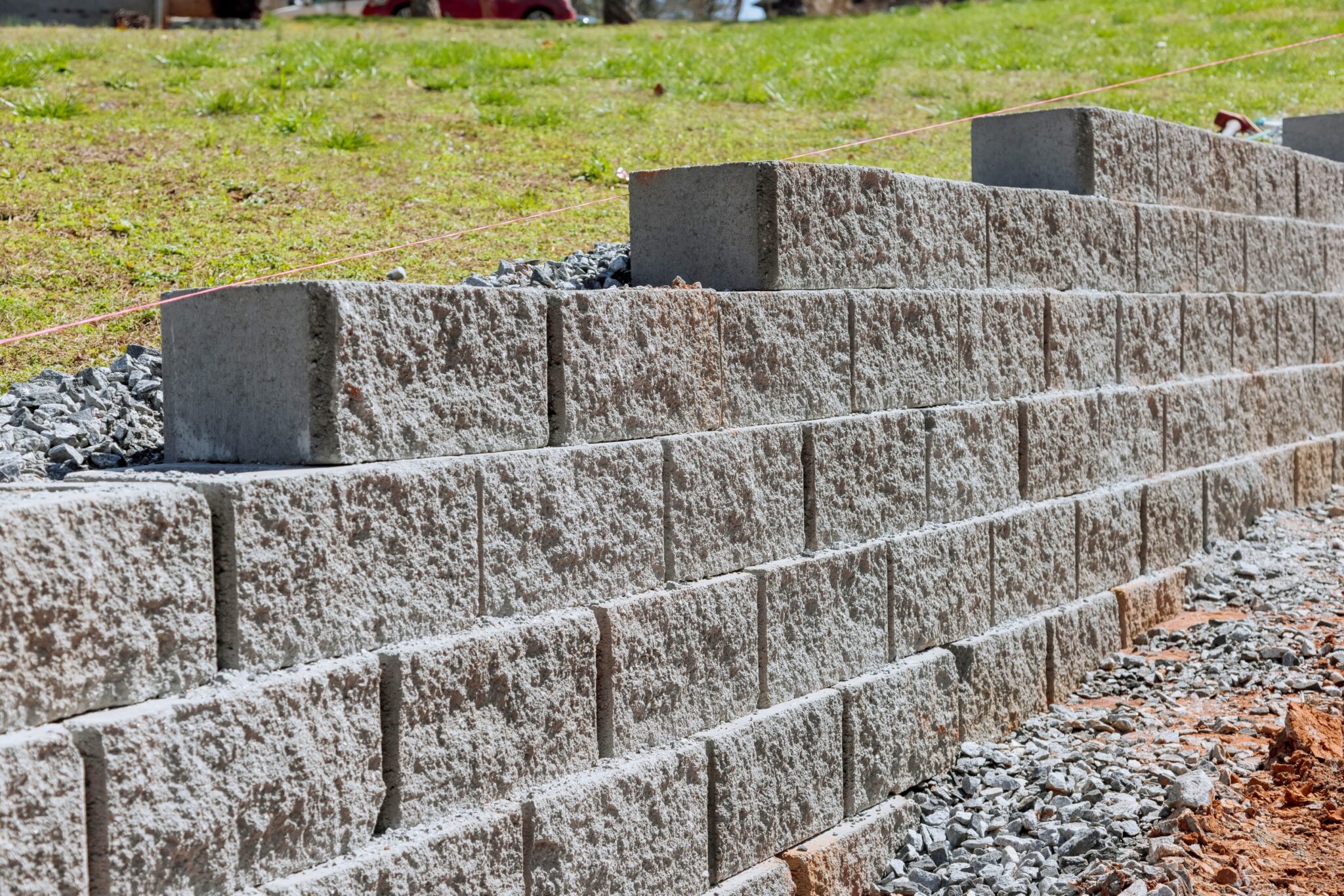 Concrete block retaining wall under construction with gravel drainage backfill behind the blocks and a string line for levelling