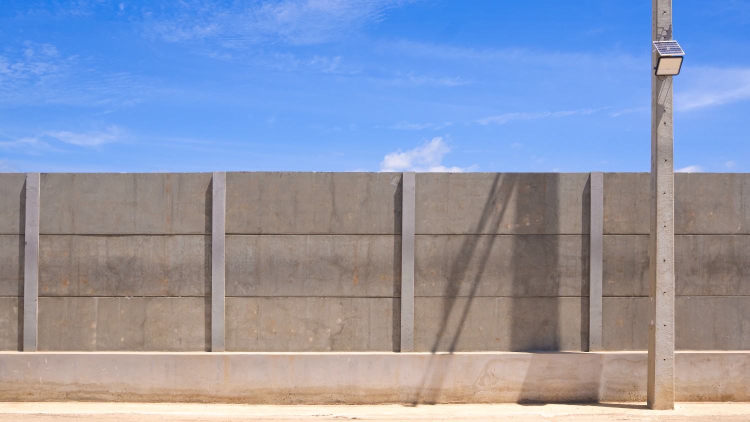 Precast concrete panel wall standing against a clear blue sky, with a solar-powered light pole alongside